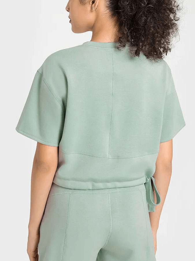 Back view of woman wearing green short sleeves crop T-shirt with adjustable hem, ideal for fitness activities.